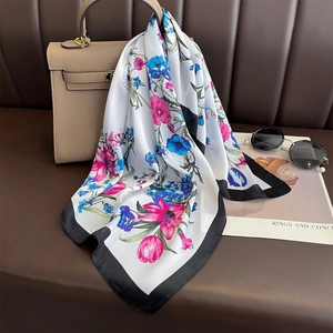 Floral silk-like scarf with black border draped on a stylish beige handbag decor