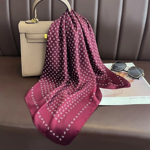 Foulard di seta bordeaux con stampa paisley annodato a una borsa a mano beige