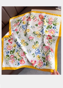 Macro shot of silk-like floral square scarf with gold border on a leather sofa