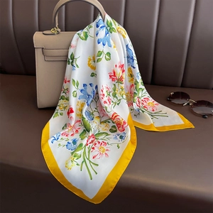 Floral print square silk scarf with yellow edges draped on a beige handbag
