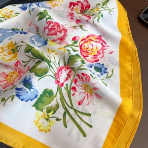 Detail of floral print silk scarf featuring a bright yellow border and smooth texture