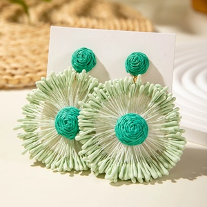 Macro detail of handmade woven raffia flower earrings in teal and mint green colors
