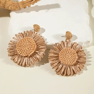 Detail of handmade raffia sunflower earrings with natural woven texture and straw finish