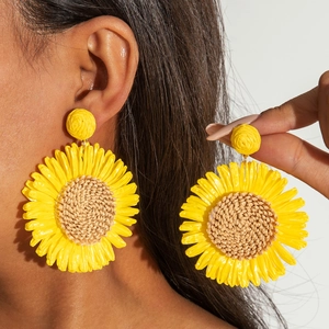 Detail of handmade yellow raffia sunflower earrings with woven texture for beach vacation