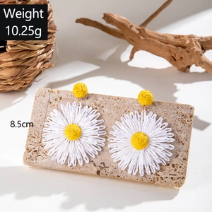 Detail showing dimensions of handmade raffia daisy earrings on a rustic stone background