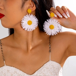 Detail shot of oversized woven raffia daisy earrings with yellow center and white petals