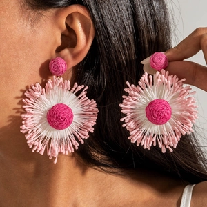 Close-up of handmade raffia flower earrings in vibrant pink and rose tones on a model