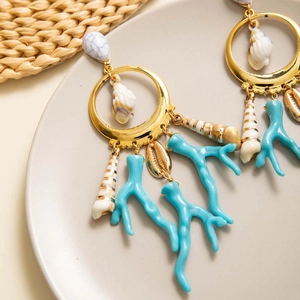 Detalle de pendientes de aro dorados con coral azul y colgantes de conchas naturales