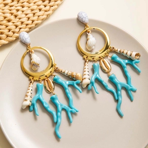 Detalle de pendientes boho dorados con ramas de coral azul y conchas naturales