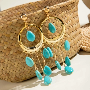Detalle de pendientes bohemios dorados con turquesas colgados en una cesta tejida