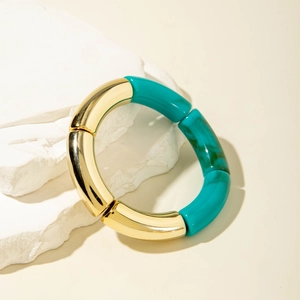 Close-up of a marbled turquoise acrylic and gold tube bracelet on white stone