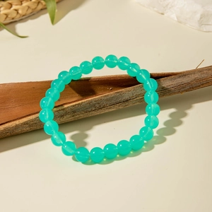 Detailed close-up of mint green acrylic beaded bracelet on a dark rustic wood branch