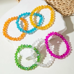 Close-up of seven colorful faceted acrylic beaded elastic bracelets on a stone tray