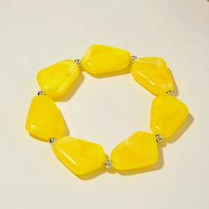 Détail de perles en résine jaune irrégulières et billes argentées sur bracelet élastique