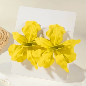 Detail of bright yellow 3D floral earrings with irregular petals on white marble stand