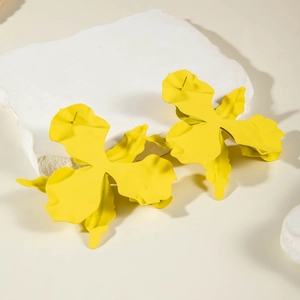 Detailed shot of bright yellow matte floral earrings on a white textured stone background