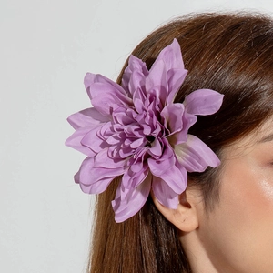 Gros plan d'une pince à cheveux fleur en tissu violet 3D portée sur le côté