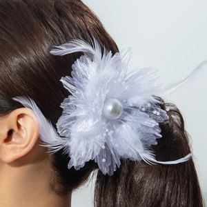 Détail d'une pince à fleurs blanches avec plumes et perle sur une queue de cheval