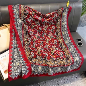 Detailed view of red paisley print scarf draped on a sofa with fashion accessories