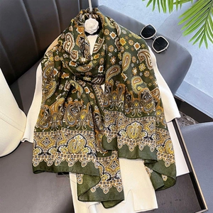 Detail of dark green paisley scarf draped on white knitwear with elegant accessories