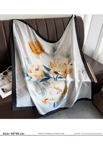 Detail of 90x90cm printed faux silk scarf draped over a leather sofa with floral patterns