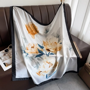 Elegant floral silk scarf featuring peony prints and black border on a leather sofa
