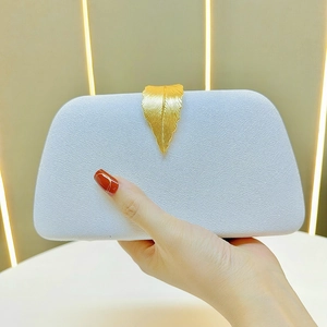 Detail of velvet evening clutch featuring a golden leaf clasp and textured finish