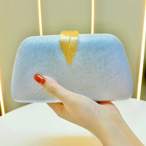 Detail view of the silver textured surface and golden leaf-shaped metal clasp on the clutch