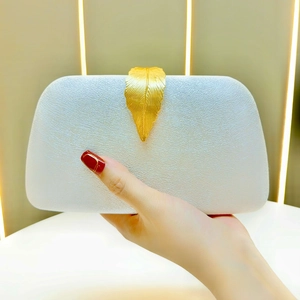 Close-up of white velvet evening clutch featuring a decorative gold leaf metal clasp