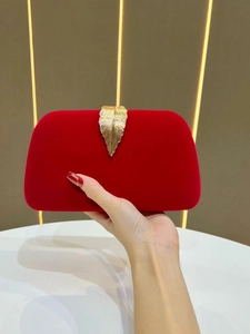 Close-up of elegant red velvet evening clutch with a luxury gold leaf-shaped metal clasp