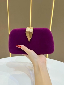 Detail of purple velvet evening clutch featuring an ornate gold leaf metal clasp