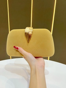 Detail of yellow velvet evening clutch featuring a golden leaf-shaped metal clasp