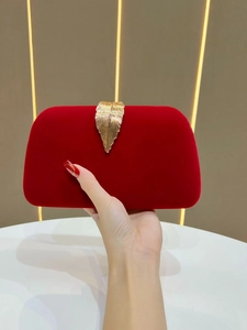 Close-up of a red velvet evening clutch with a golden leaf clasp held by a person