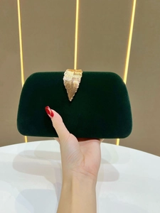 Detail of dark green velvet clutch bag featuring a luxurious golden leaf-textured clasp