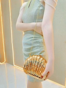 Detail of a gold shell-shaped evening bag with radial texture and metal chain