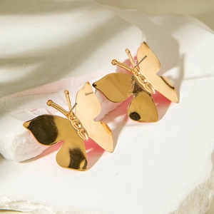 Gros plan détaillé de boucles d'oreilles papillon dorées sur une pierre texturée blanche
