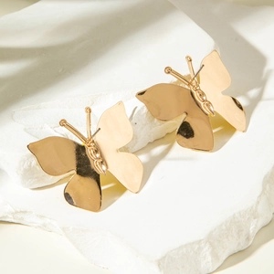 Détail des boucles d'oreilles papillon dorées avec finition polie sur une surface en pierre