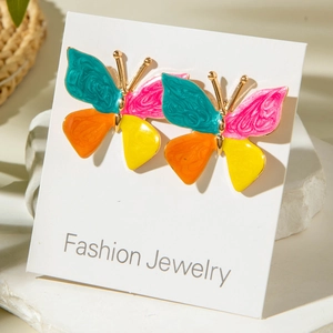 Détail de boucles d'oreilles papillon en émail coloré sur un plateau de pierre blanche