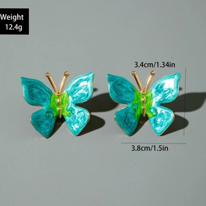 Détail de grandes boucles d'oreilles papillon en émail bleu et vert avec bords dorés