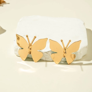 Vue détaillée des boucles d'oreilles papillon dorées sur une surface en pierre blanche