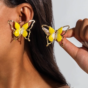 Gros plan d'une boucle d'oreille papillon jaune avec cadre doré porté par un modèle