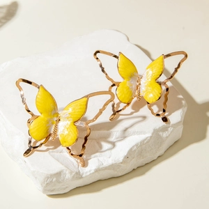 Détail de boucles d'oreilles papillon dorées avec émail jaune sur support en pierre