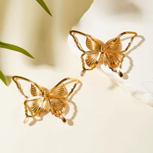 Gros plan détaillé de boucles d'oreilles papillon dorées avec ailes gravées sur socle pierre
