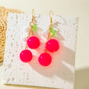 Detailed macro shot of red cherry and white lily of the valley earrings with gold metal hooks