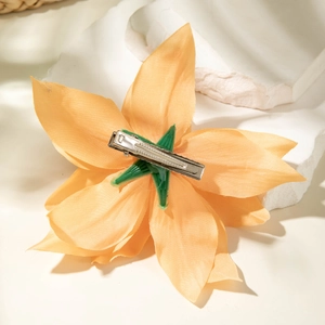 Detailed back view of orange lily hair clip showing silver metal duckbill clip and green base