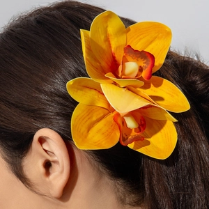 Detailed view of a yellow and orange lily flower hair clip worn on long dark hair