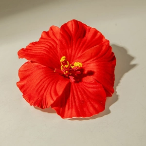 Detailed close-up of a red tropical lily hair clip with yellow stamen and lifelike texture