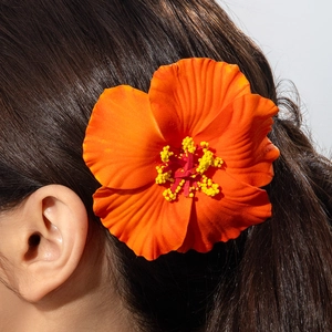 Detail of vibrant orange hibiscus flower hair clip with yellow stamen on black hair