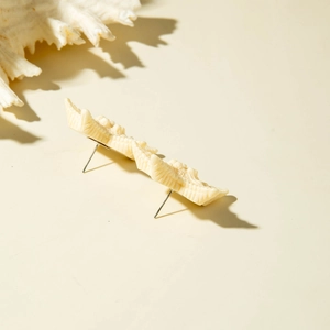 Detailed view of cream textured resin starfish earrings with shell props on a beige background