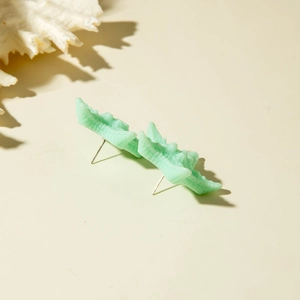 Detail shot of mint green crocodile-shaped resin stud earrings on a beach-themed background